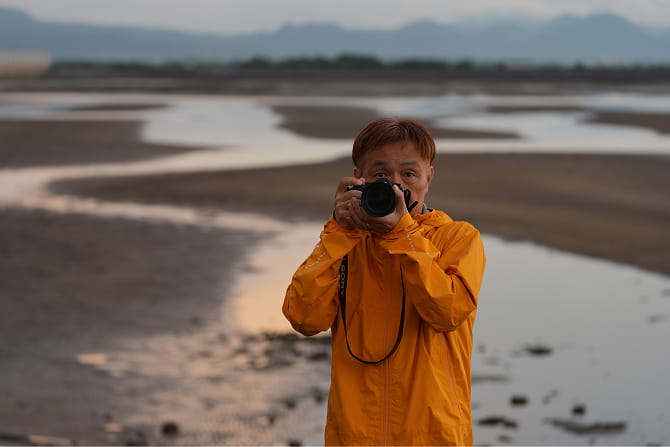 河原でカメラを構える写真家 Kazu Kobayashi